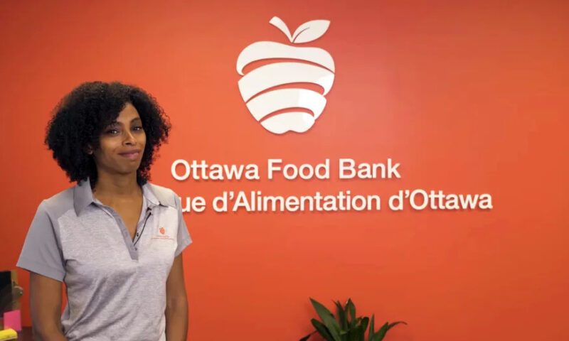 A woman stands in front of a red wall that reads, "Ottawa Food Bank" with its French translation below.