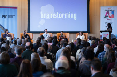 Audience watches panel of five seated individuals on stage in front of screen that reads "brainstorming"