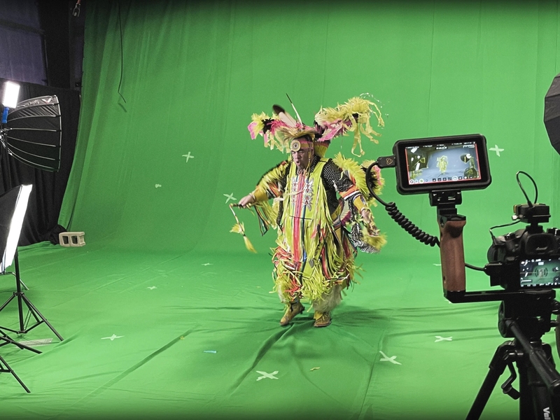 Dancer in Indigenous ceremonial dress front of a green screen